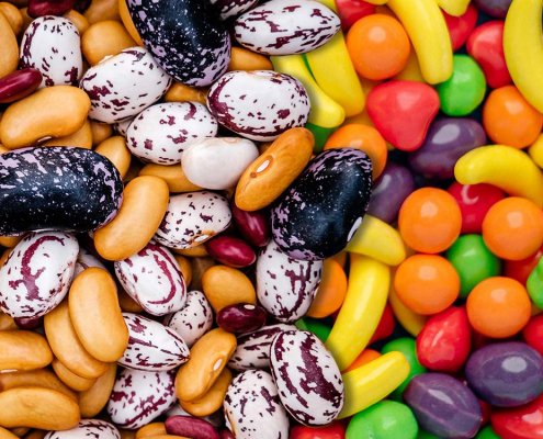 Close up view of a pile of beans on the left side, composited with a pile of candies on the right.
